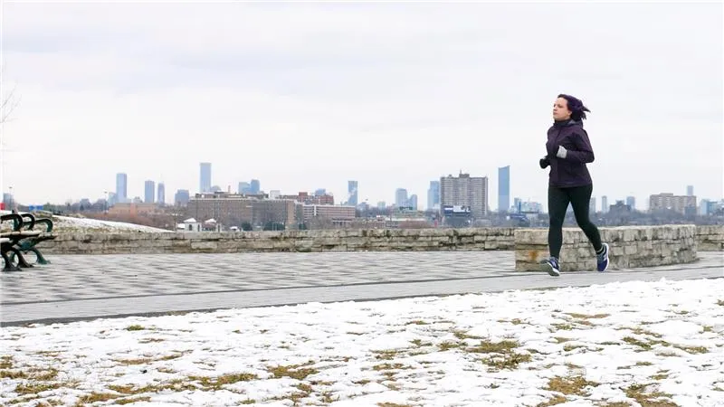 A woman jogging on a snowy path with a city skyline in the background